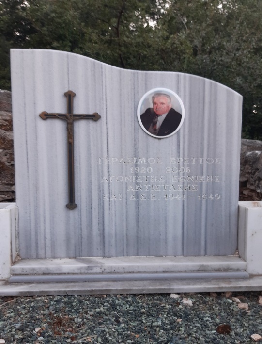 Detail of a tomb with an upright marble slab bearing a metal cross, a photograph of a middle-aged man and a text.